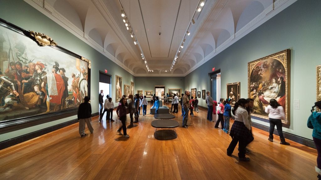 Visitors explore a gallery with large classical paintings, arched ceilings, and polished wooden floors in the Art Gallery of Ontario.