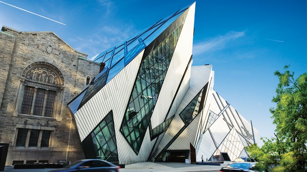 Modern glass-and-metal facade of the Royal Ontario Museum contrasts with historic stone architecture beside it under a clear blue sky.