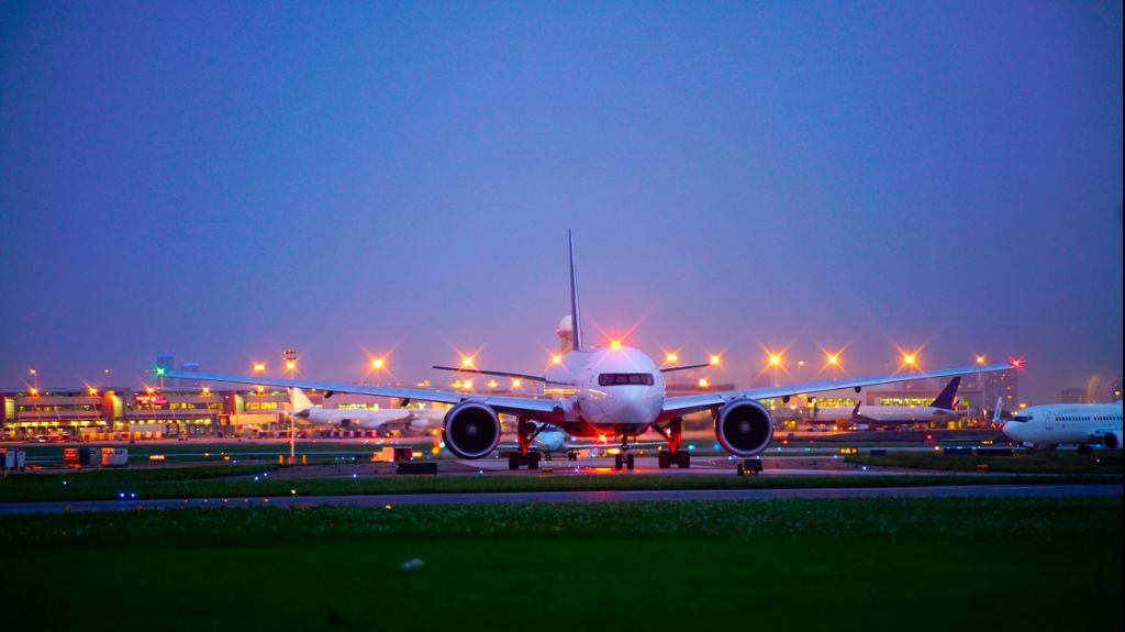 Front view of a large passenger plane on a runway at dusk, with airport lights and terminals in the background.