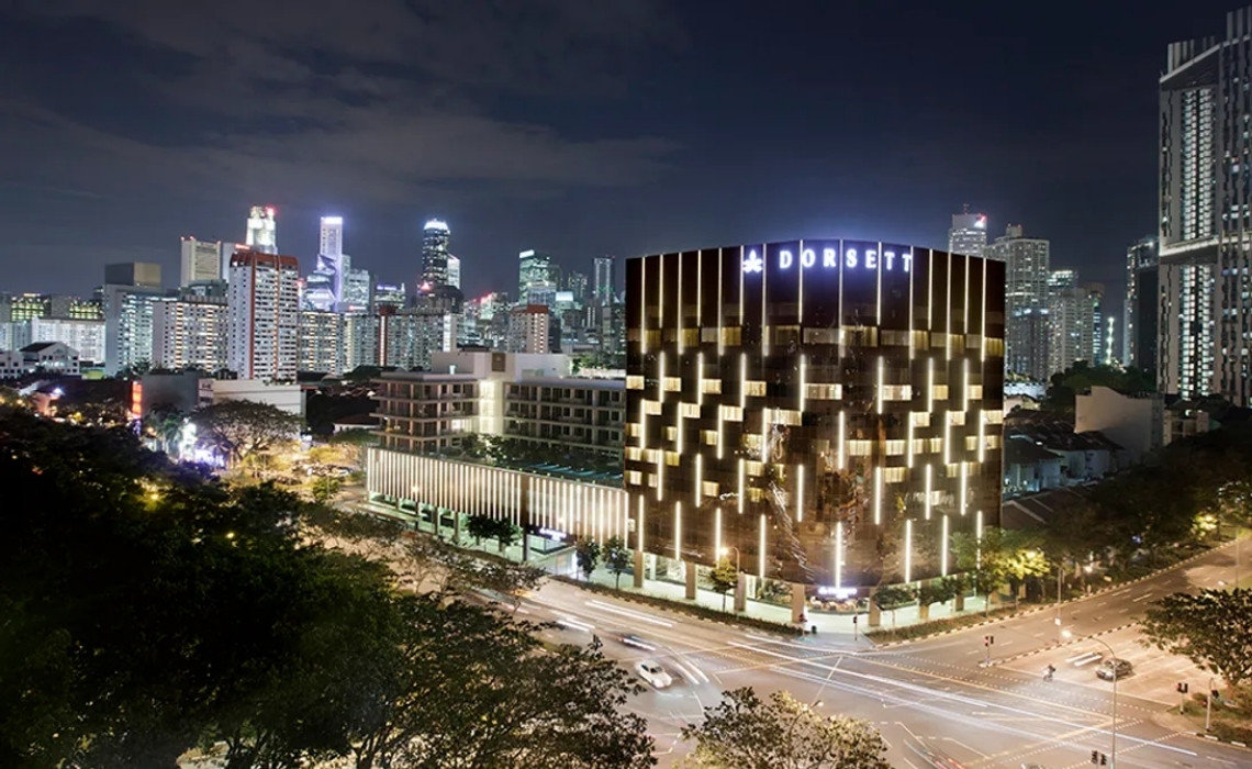 Dorsett Hotel lit up at night with Singapore’s city skyline in the background and traffic on surrounding roads.