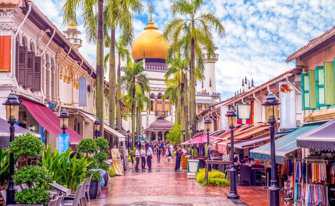 Colorful street lined with shops and palm trees, leading to Sultan Mosque with its golden dome in Singapore’s Kampong Glam.