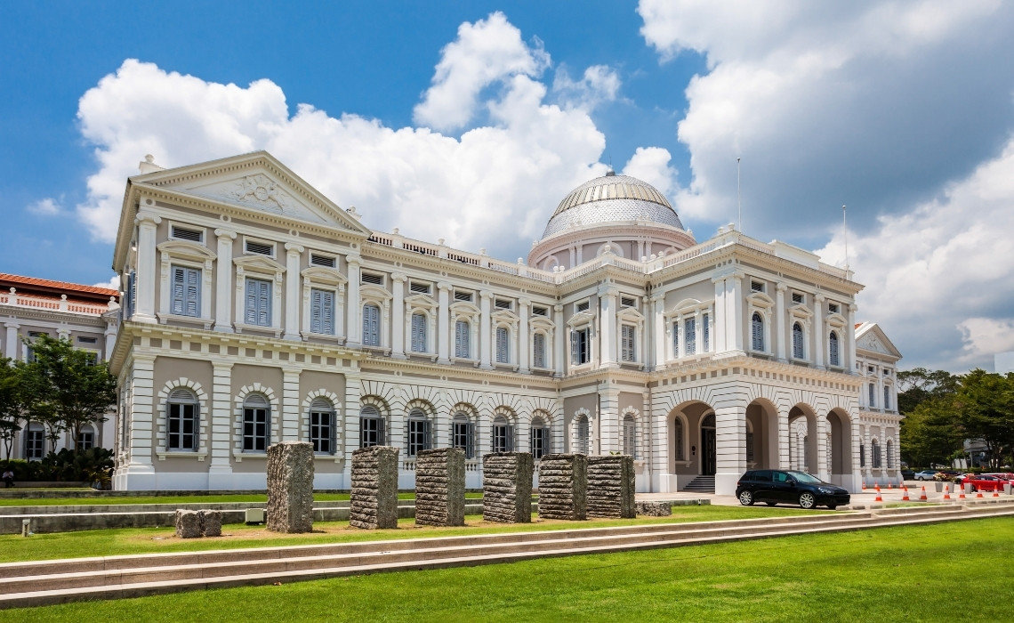 The National Museum of Singapore with its neoclassical architecture, dome, and stone sculptures on a bright sunny day.