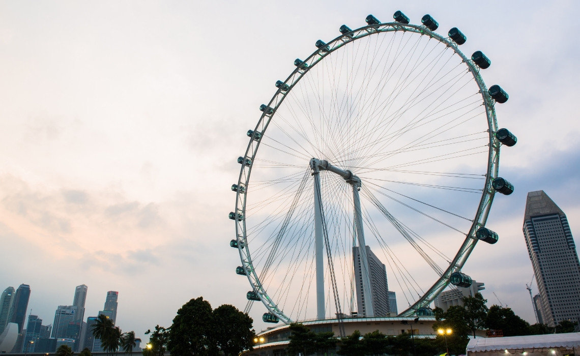 The Singapore Flyer giant observation wheel with city skyscrapers in the background during a cloudy sunset.