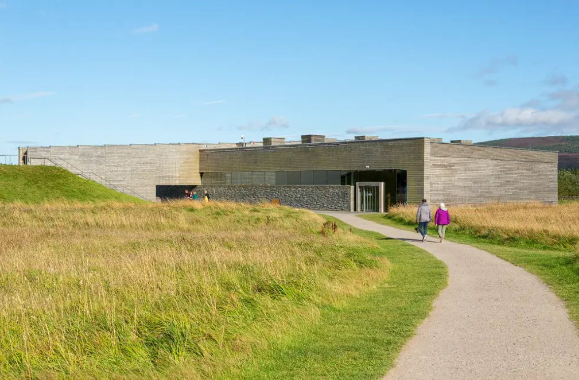 Culloden Battlefield Visitor Centre, modern low building in grassy moorland under clear skies.