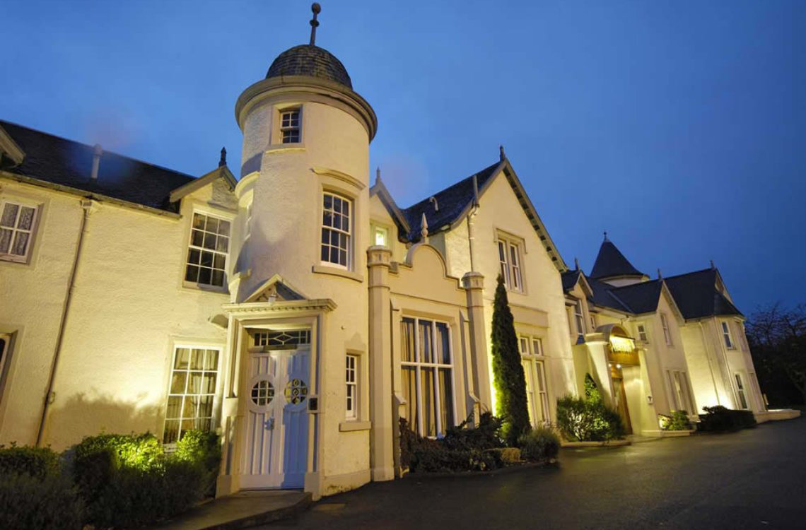 The Kingsmill Hotel. Elegant white-fronted mansion hotel in Inverness with turret and warm lighting against a deep blue evening sky.